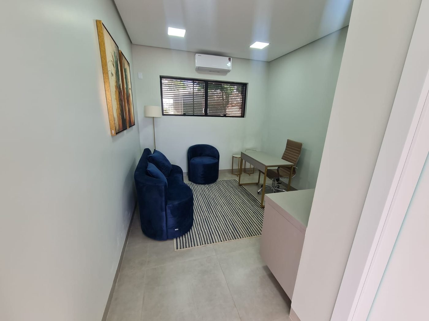 Sala de atendimento com poltronas, luminária de piso e mesa de trabalho